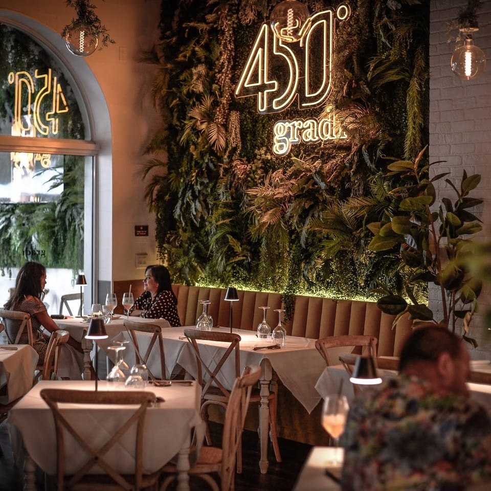 Elegant 45 Gradi restaurant dining room with white tablecloths, greenery-covered wall, glowing neon sign, and seated diners.